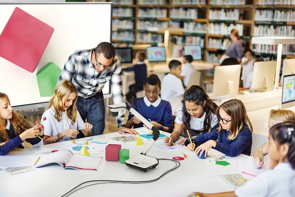 Lehrer und Schülerinnen arbeiten mit einer Dokumentenkamera am Tisch